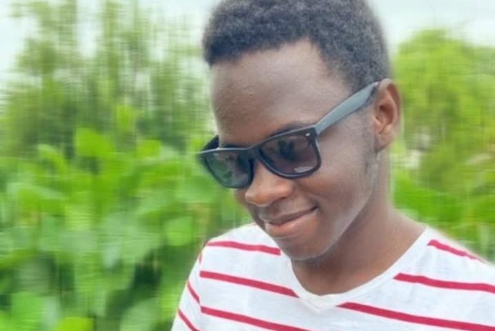image of Benjamin Shikusho, he wears a white T-Shirt with red stripes. he is wearing black shades and has a smile.