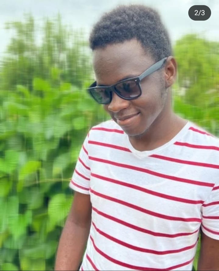 image of Benjamin Shikusho, wearing black shades, white t-shirt with red lines, he appears to be smilling facin slight right with his head slanted slighly towards the right aswell
